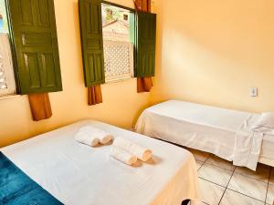 two beds in a room with green windows and towels at Casa de Nara in Lençóis