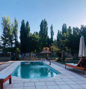 a swimming pool with an umbrella and a table and benches at Cabañas El bosque DLM in Uspallata