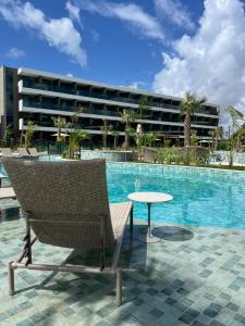a chair and a table next to a swimming pool at Novíssimo Flat Beach Class Solare - Muro Alto -Soft Open in Porto De Galinhas