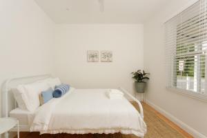 a white bedroom with a white bed and a window at Greta Cottage, Berry in Berry