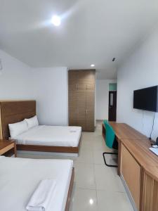 a room with two beds and a desk and a tv at Hotel Training Center UIN Mataram in Mataram