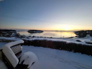 a bench covered in snow with the sunset in the background at Koselig feriehus ved sjøen - Skjevikstranden in Steinkjer