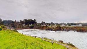 a river with a fence next to a grassy field at Windrose in Fort Bragg