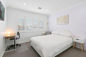 a white bedroom with a bed and a desk at Saltwater Cottage in Windang
