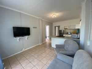 a living room with a couch and a tv and a kitchen at Beach Cresent Cottage in Port Alfred