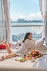 a woman laying on a bed with a tray of food at DeLaSea Ha Long Hotel - Modern Bayview Escape in Ha Long +143 photos