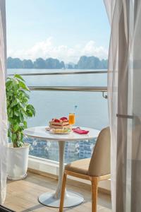 a table with a plate of food and a drink on a balcony at DeLaSea Ha Long Hotel - Modern Bayview Escape in Ha Long