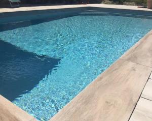 a swimming pool with blue water and a wooden floor at Chambre Au clos des auges in Saint-Saturnin-du-Bois