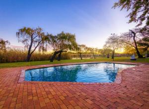 a swimming pool in a park with a brick patio at Riverside Rhapsody, Vaal River, Vanderbijlpark, 6 Adults and 4 Children in Vanderbijlpark
