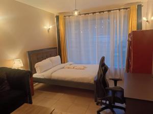 a bedroom with a bed and a chair and a window at Legatus Cozy Studios B - Ongata Rongai Furnished Apartment with Swimming pool in Nairobi