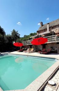 a swimming pool with red umbrellas and chairs at Chambres d'hôtes Les Violles in Chirac