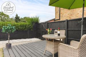 a table and chairs on a wooden deck with an umbrella at Luxury 2-Bed House in Stevenage Sleeps 6 Free Parking Barefoot & Board in Shephall