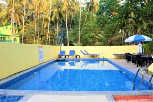a swimming pool with chairs and a table and an umbrella at Sonikas Holiday Homes (Studio) in Candolim