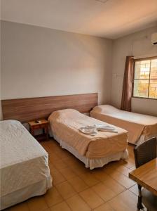 ein Schlafzimmer mit zwei Betten, einem Tisch und einem Fenster in der Unterkunft Hotel Brivanna in Campo Grande