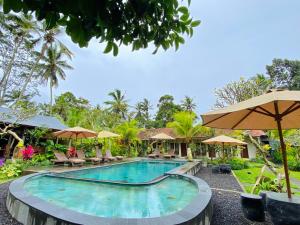 a pool at a resort with chairs and umbrellas at Puri Kurnia Ayu in Ubud