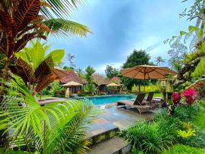 a swimming pool with two chairs and an umbrella at Puri Kurnia Ayu in Ubud