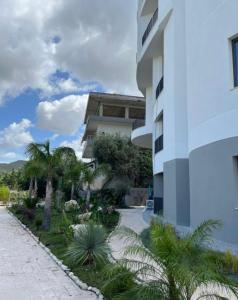 a white building with palm trees next to a sidewalk at Dior Apartment in Vlorë