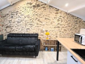 a living room with a black couch in front of a stone wall at La Dilettante - petit déjeuner inclus - 10mn du Parc in Treize-Vents