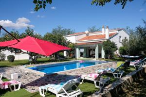 a house with a swimming pool with chairs and a red umbrella at Villa Vinko in Donje Raštane