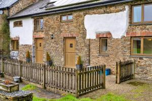 a stone house with a wooden fence in front of it at Finest Retreats - Oak Leaf Cottage in Beaworthy