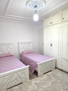 a white bedroom with two beds and a chandelier at إقامة الكرنيش in Nador +7 photos