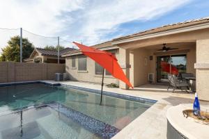 a red umbrella in a swimming pool with a house at Copper Cactus House Pool, Spa, Golf! in Queen Creek