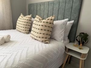 a bed with white pillows and a gray headboard at Saviour Apartments in Mthatha