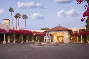 a building with a fountain and palm trees and pink flowers at The Scottsdale Resort & Spa, Curio Collection by Hilton in Scottsdale