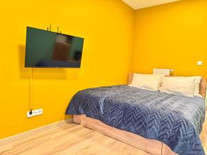 a bedroom with a bed and a tv on a yellow wall at Rumia Apartment by JumpInHere in Rumia