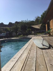 a surfboard sitting on a wooden bench next to a swimming pool at La tranquille marée , à 5 min des plages in Soorts-Hossegor