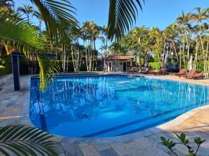 a swimming pool with blue water and palm trees at Apartamento em Maresias a 100 metros da praia in Maresias