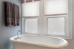 a white bath tub in a bathroom with two windows at Steps to Dtwn Plymouth! Home w/ Dog-Friendly Yard in Plymouth +25 photos