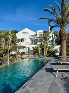 a swimming pool in front of a house with palm trees at Casa Caloura Passion Deluxe Accommodation & Spa in Lagoa