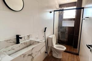 a white bathroom with a toilet and a shower at Charlotte Beach Inn in Mangaratiba
