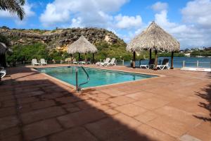 a swimming pool with chairs and umbrellas and the ocean at Beach front luxury living - 2 bedroom condo with sea view in Jan Thiel