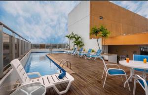 a pool on the roof of a building with chairs and tables at Flat hotel Blue tree no adrianopolis Até 4 pessoas in Manaus