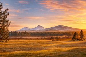 a field with a fence and mountains in the background at Lodge Room 018 in Black Butte Ranch