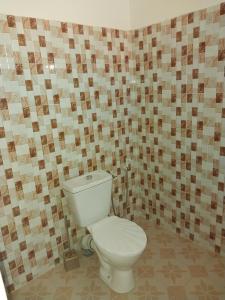 a bathroom with a toilet and a tiled wall at Keur Fall Aéroport in Saint-Louis