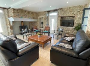 a living room with leather furniture and a stone wall at Gite du coos in Audaux