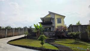 a yellow house with a fence and a yard at Mroom Villa Cipanas in Pacet