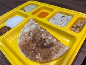 a yellow lunch box with a pancake and other foods at Le Park Luxury Resort - TIE Hotels in Pondicherry