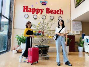 two women standing in front of a happy beach sign with luggage at Happy Beach Hotel in Nha Trang