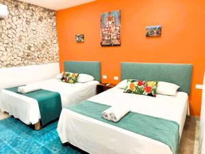 two beds in a room with an orange wall at Casa colonial tranquila cerca del centro, Casa Solecito in Valladolid