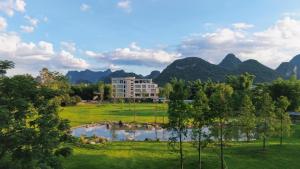 ein Gebäude auf einem Feld mit einem See und Bergen in der Unterkunft YINGMAN HOTEL in Yangshuo