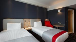 a hotel room with two beds and a red chair at Holiday Inn Express Geneva Airport by IHG in Geneva +18 photos