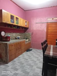 a kitchen with pink walls and wooden cabinets and a table at Jupe Homestay batukaras in Batukaras