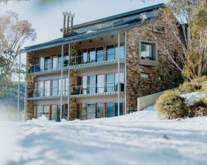 a building with snow in front of it at Alpine Woodsmoke Apartments in Falls Creek