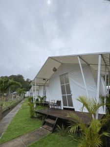 a white house with awning and benches on a lawn at Ohara Glamping in Kubupenlokan