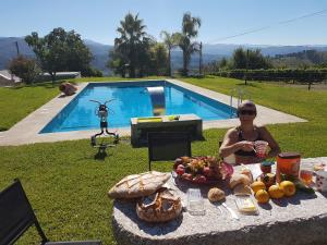 a woman sitting in front of a table with food and a pool at Quinta de Santa Marinha in Arcos de Valdevez