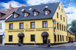 a yellow building with a black roof on a street at Penzion, restaurant Gloria in Chrastava